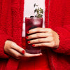 Cocktail served in the Highball glass held by someone wearing red jacket and pants.