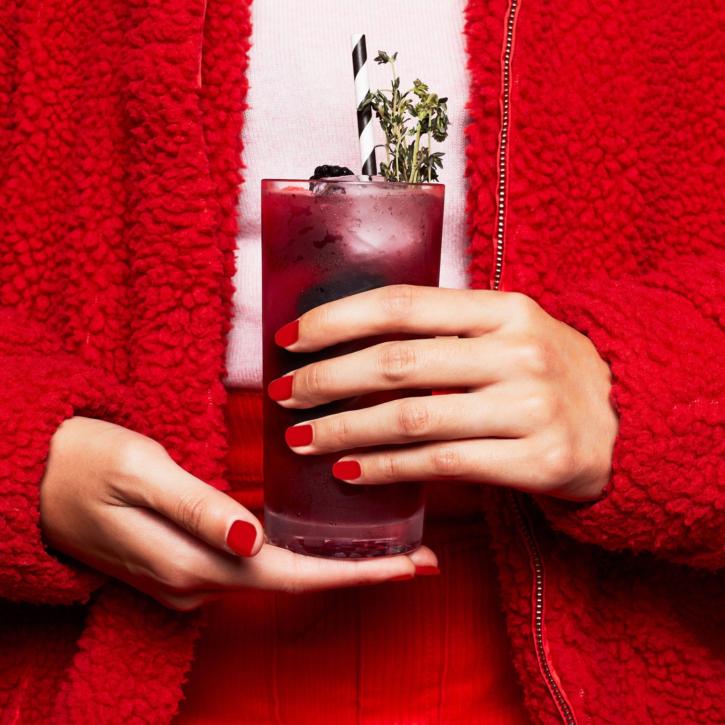 Cocktail served in the Highball glass held by someone wearing red jacket and pants.